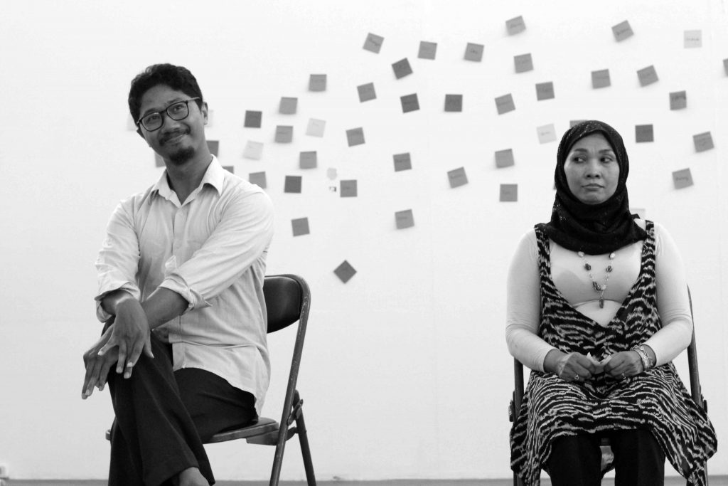 Two people sit on folding chairs, a man looking smug and a woman looking skeptical.