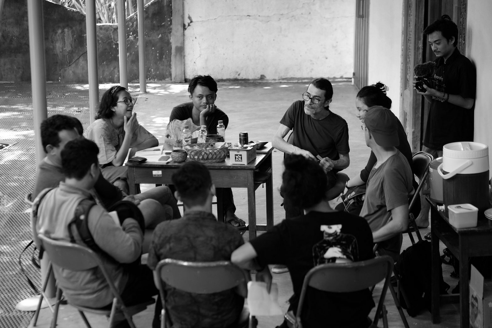 Pertemuan produksi dengan Caglar dan kru yang duduk di sekitar meja / Production meeting with Caglar and crew sitting around a table