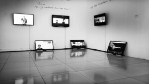Exhibition view of video installation with monitors hung on walls and resting on the floor.