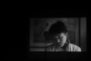 Projected video of a pensive young man seen from the shoulders up.