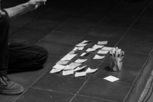 Post it notes stuck to the floor next to a container of pens and someone’s knee and foot.